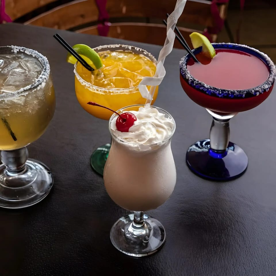 Four vibrant Dos Charros drinks: two margaritas, a creamy cocktail with a cherry, and a red drink.
