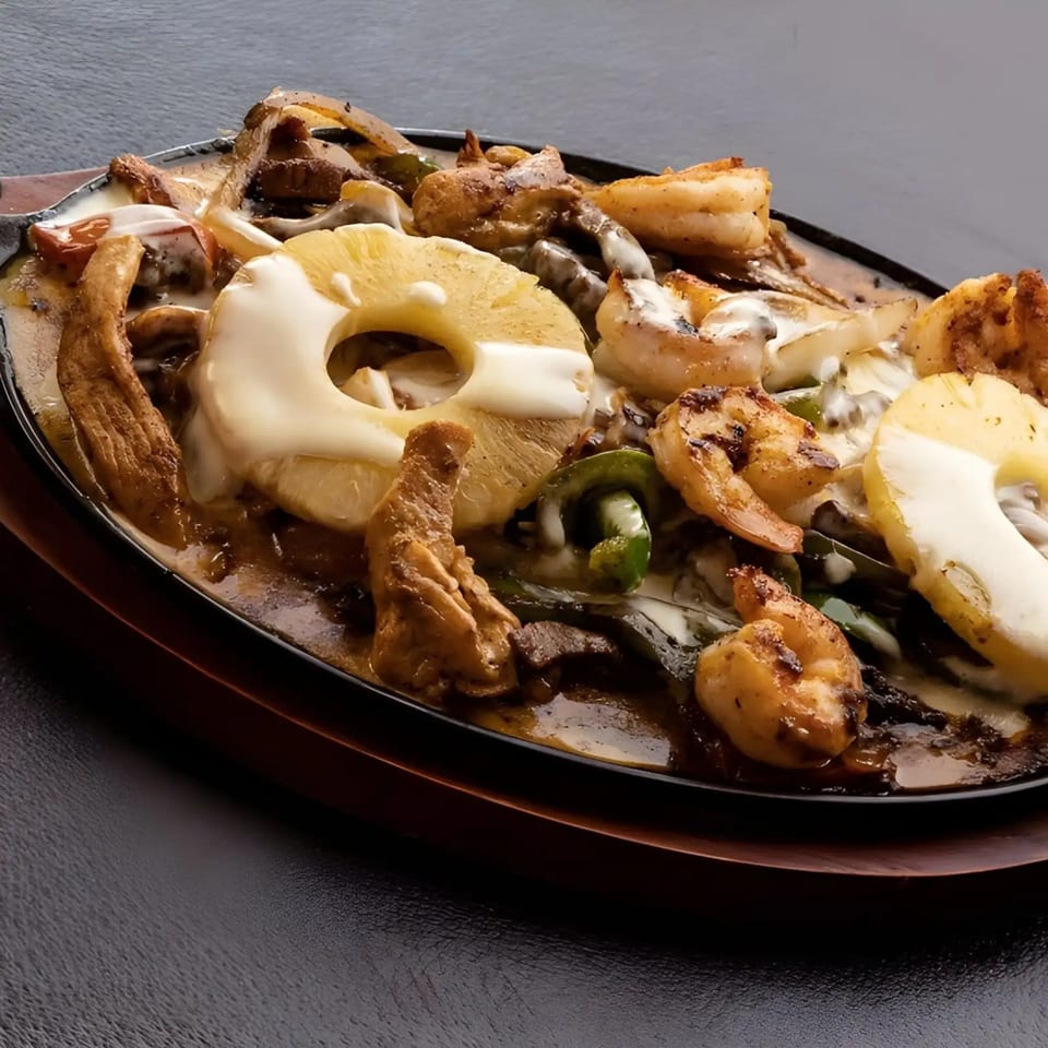 Dos Charros sizzling fajita platter with shrimp, chicken, steak, pineapple, and melted cheese.